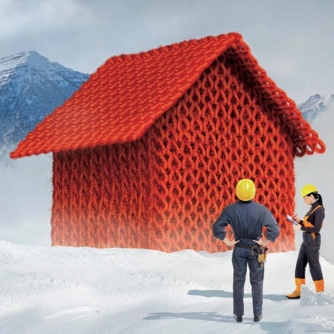 Ein rotes, gestricktes Haus in einer Schneelandschaft wird von einer Ingenieurin und einem Ingenieur auf die Wärmedämmung geprüft.