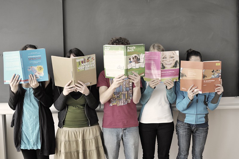Schüler*innen stehen in einer Reihe und halten sich Bücher vors Gesicht