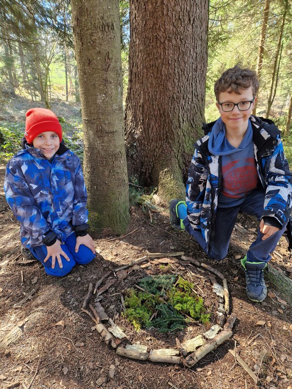 Zwei Kinder sitzen vor einem Waldmandala